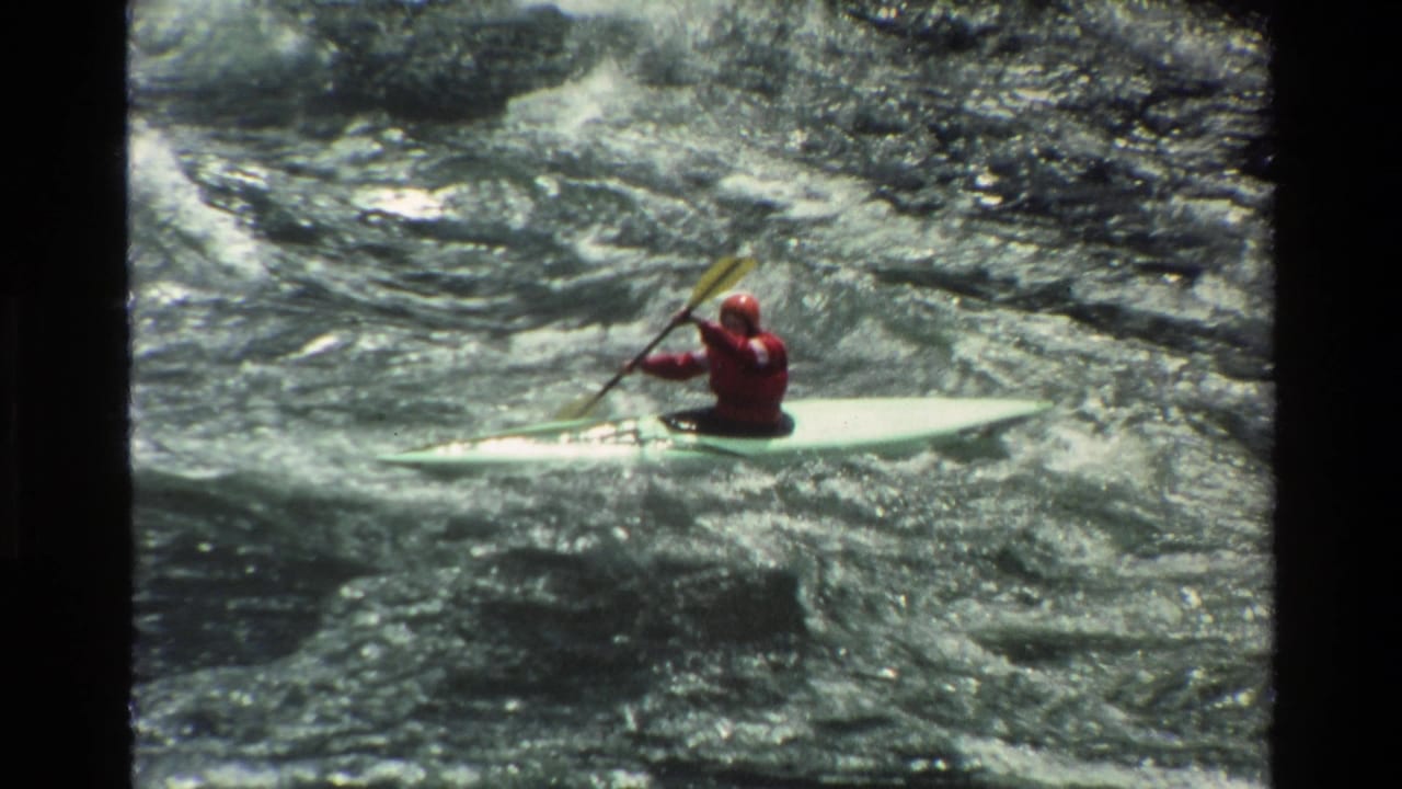 Kayaker raises a paddle while riding over turbulent water.