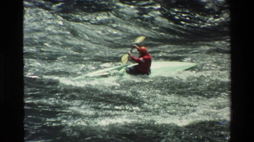 1980 Grand Teton frame showing a kayaker in red gear paddling downstream through bright, choppy whitewater.
