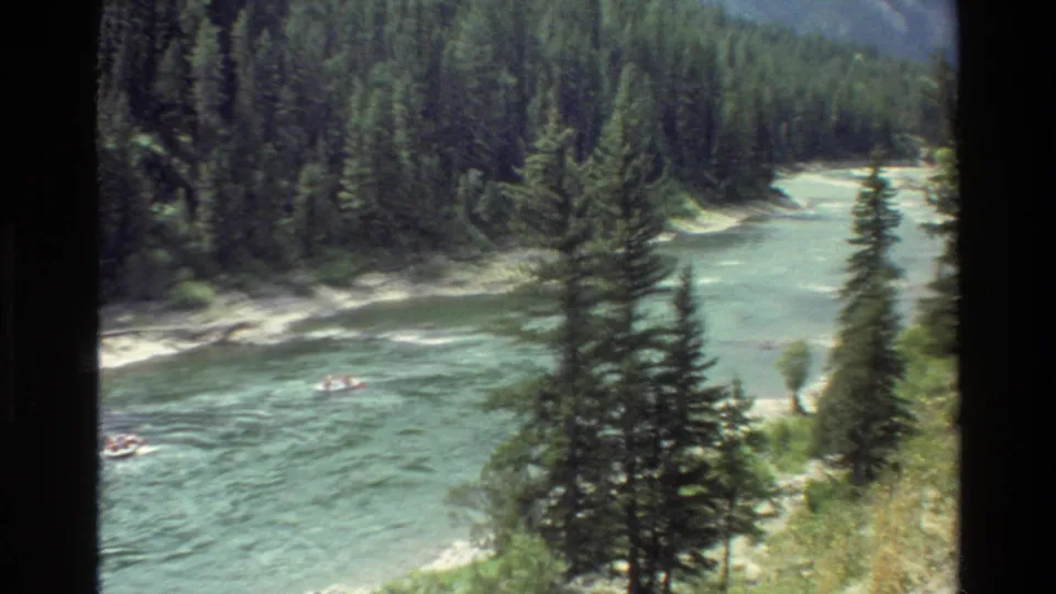 1980 Grand Teton home-movie frame of distant river floaters passing through a forested mountain waterway.