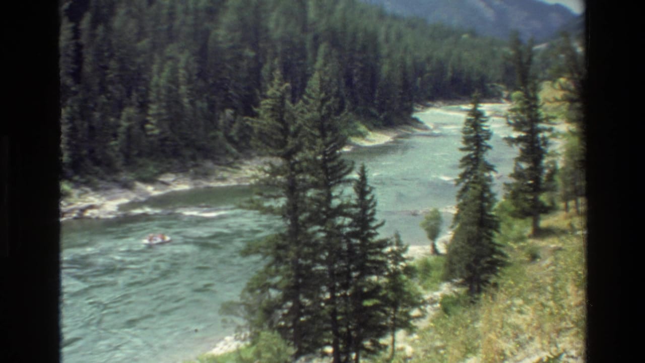 1980 Grand Teton, Wyoming home-movie frame showing a small raft on a blue-green river bordered by evergreens and mountain slopes.