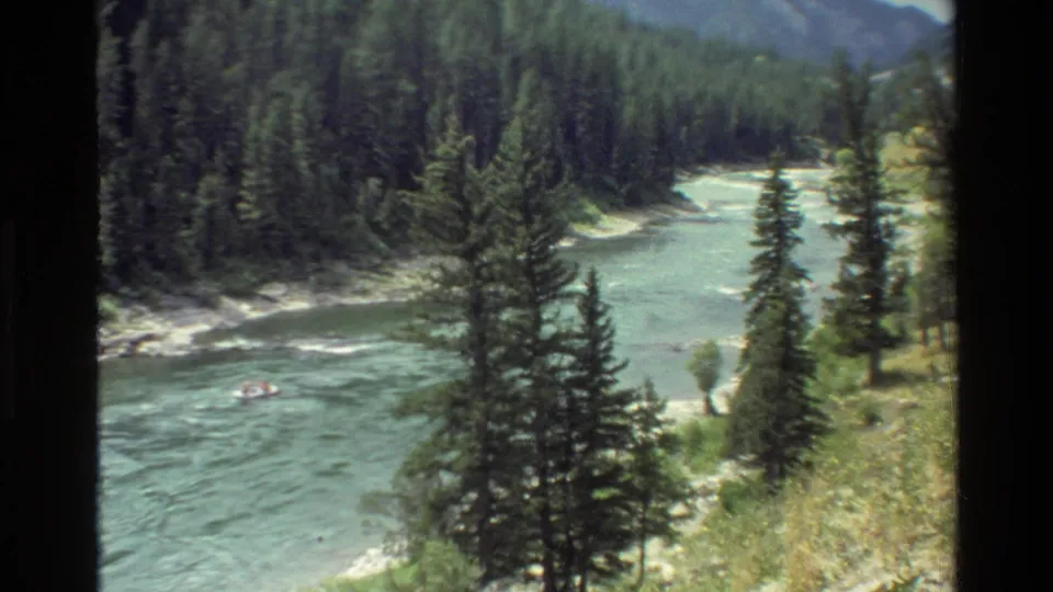 1980 Grand Teton, Wyoming home-movie frame showing a small raft on a blue-green river bordered by evergreens and mountain slopes.