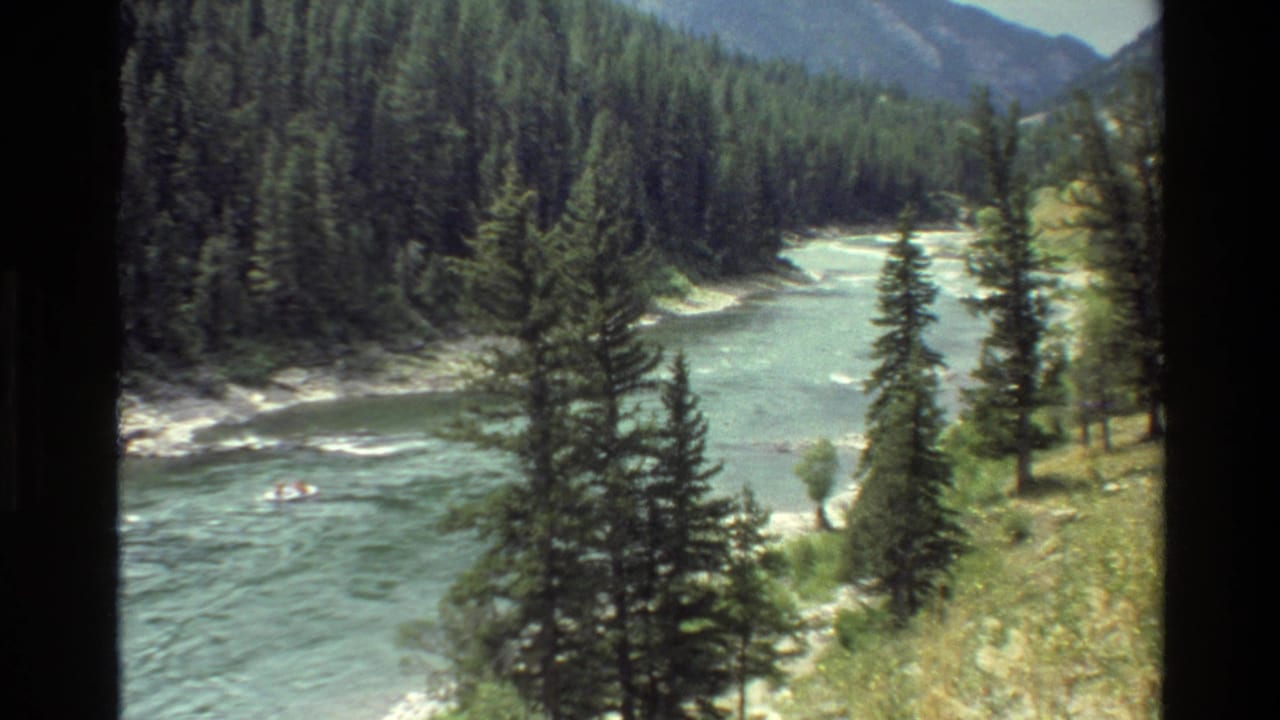 River bend below pine-covered slopes with a small raft near the left side.