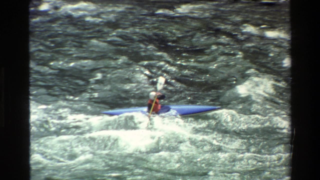 Helmeted kayaker in a blue kayak paddling through choppy whitewater.