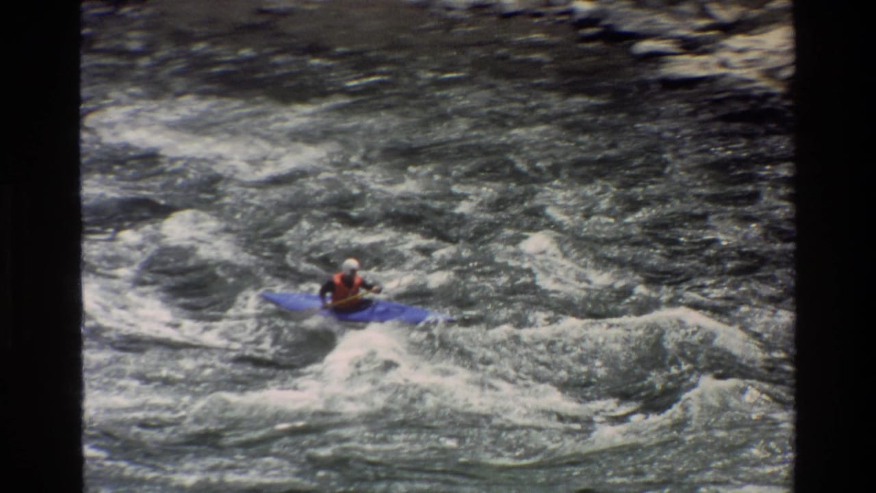 Kayaker in a blue kayak entering foamy whitewater rapids from a high angle.