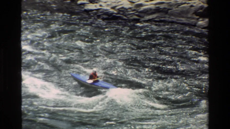 The kayaker continues through Grand Teton whitewater, with foamy current and rocks visible along the upper edge of the frame.