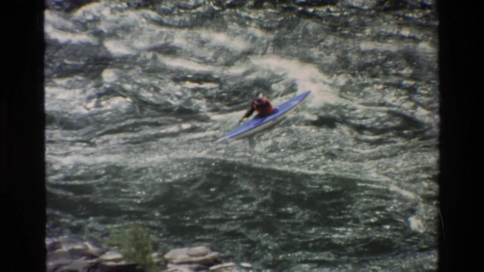 A kayaker in a blue boat navigates whitewater rapids in 1980 Grand Teton, Wyoming home-movie footage.