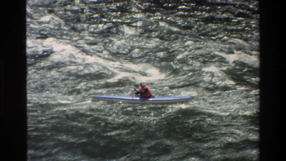 A kayaker in a blue craft passes through foaming whitewater during the 1980 Grand Teton river sequence.