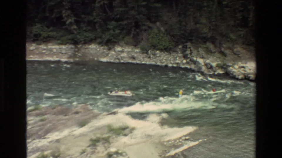 1980 Grand Teton, Wyoming wide frame showing kayakers on a turbulent river with rocky shoreline and trees beyond.