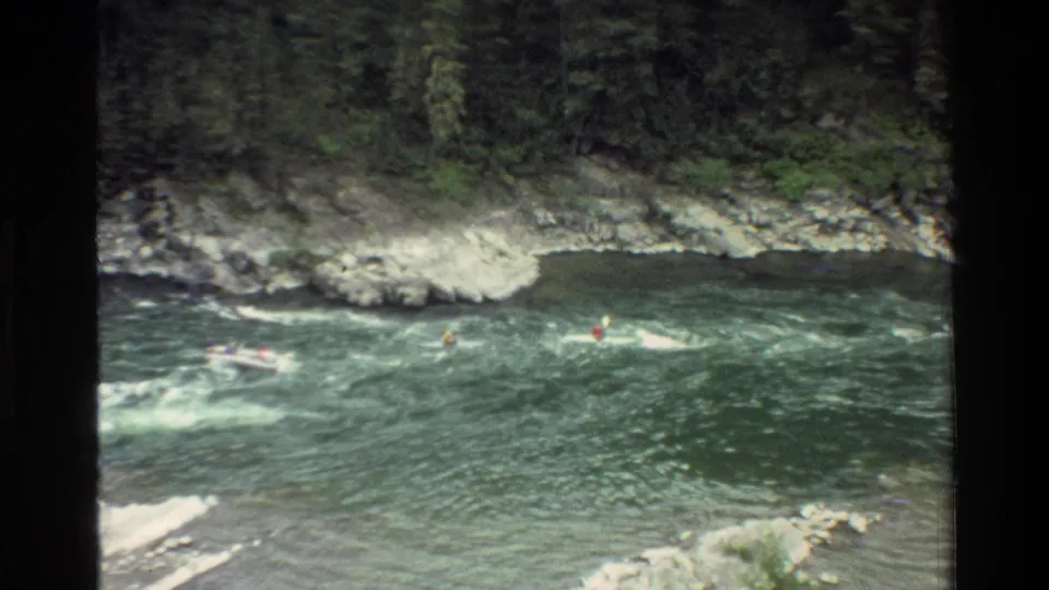 Final 1980 Grand Teton frame showing small figures in boats crossing white water with forest and rocks behind them.