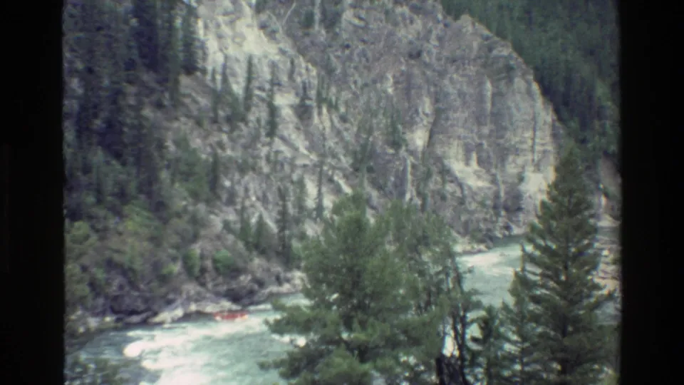 Small orange raft appears in a rushing river framed by pine trees and steep Wyoming canyon rock.
