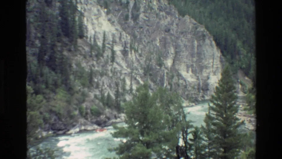 Distant raft travels through foaming water under pale canyon walls in Grand Teton-area home-movie footage.