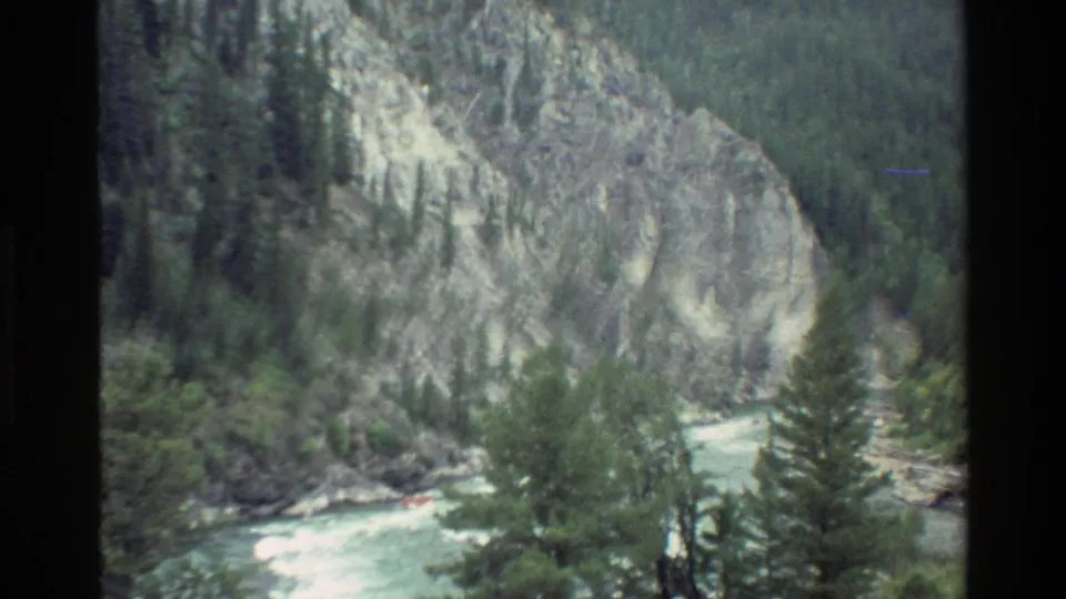 Soft final frame shows the canyon river, pines, and pale rock walls as the raft becomes hard to distinguish.