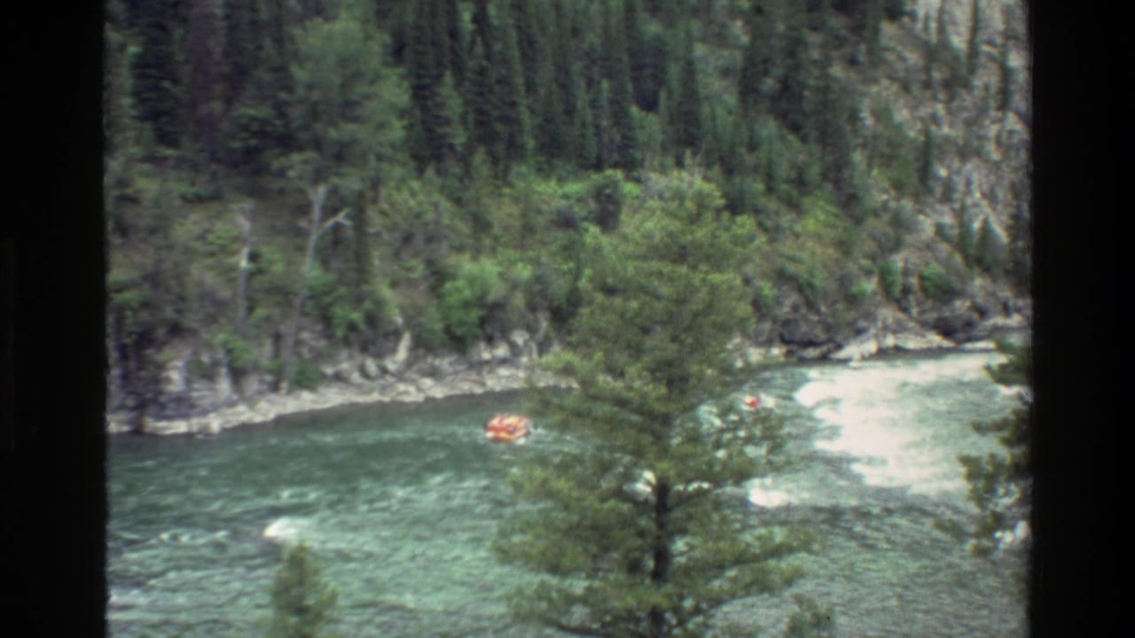 Orange raft in a bend of fast water with forest and rocks along the riverbank.