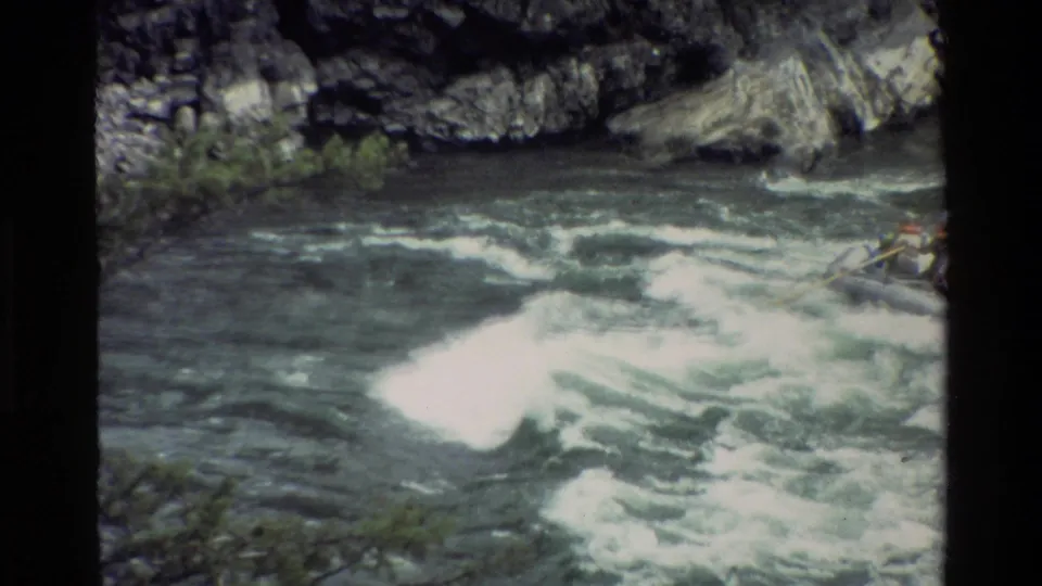 A cropped 1980 8mm frame shows turbulent green-blue water and white foam, with part of a raft and paddler entering from the right edge.