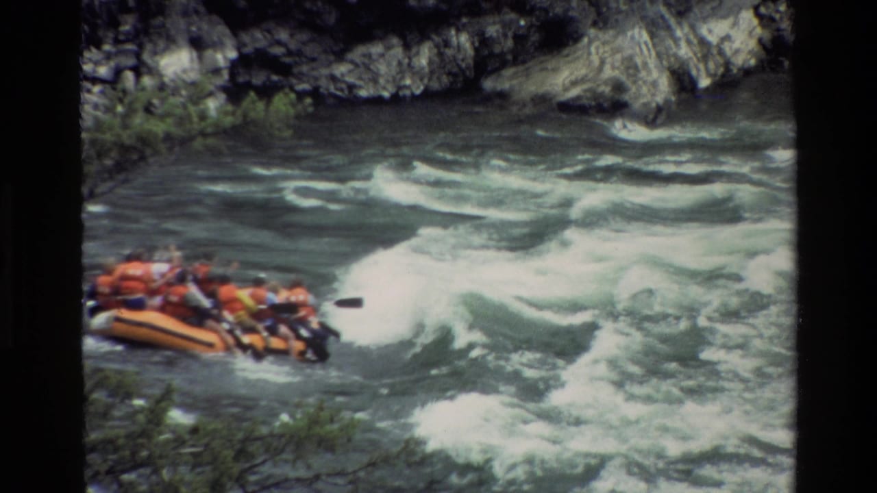 1980 8mm view of rafters in orange life jackets entering rough water in Grand Teton, Wyoming.