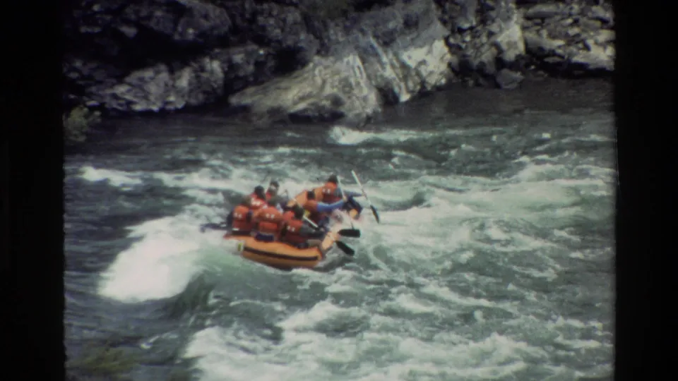 Orange-vested rafters continue downstream through turbulent water in the 1980 Wyoming rafting footage.