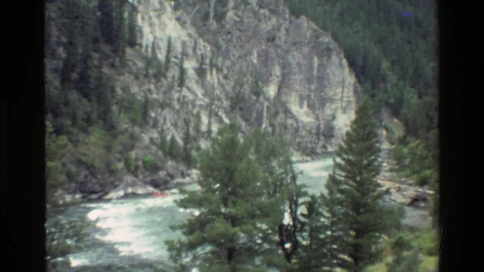 The closing frame widens to the rocky Grand Teton river canyon, with evergreen trees, bright rapids, and the raft small in the distance.