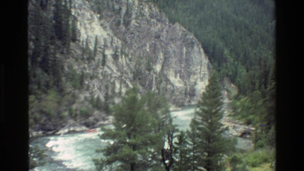 1980 Grand Teton-area home-movie view of a mountain canyon, forested slopes, and a pale river running below.