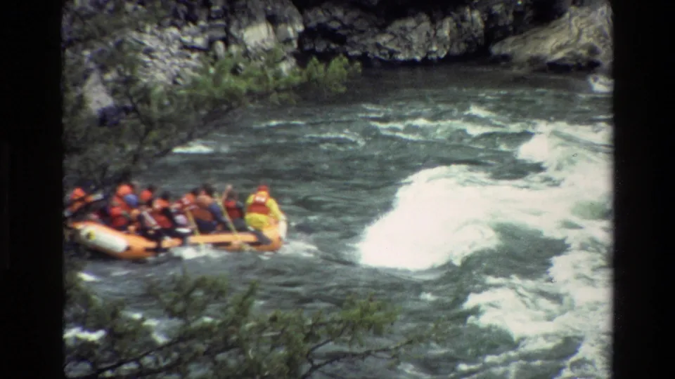 An orange whitewater raft carrying visible rafters in life jackets moves into rough water in the Grand Teton-area river canyon.