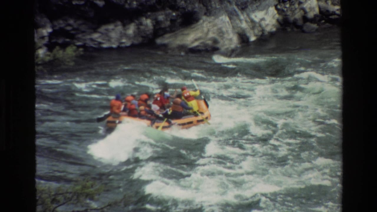 1980 Grand Teton home-movie frame of an orange raft with paddlers in life jackets riding through churning river rapids.