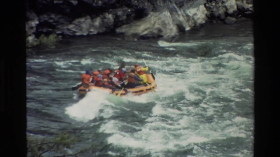 1980 Grand Teton home-movie frame of an orange raft with paddlers in life jackets riding through churning river rapids.