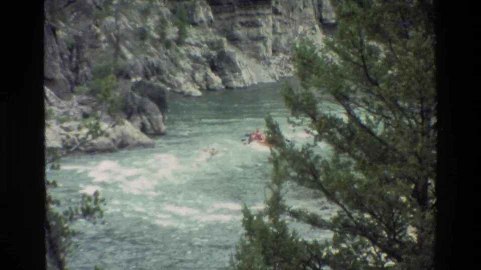 Home-movie frame of rafters farther downstream in Grand Teton, with white water, rocks, and evergreen branches in view.