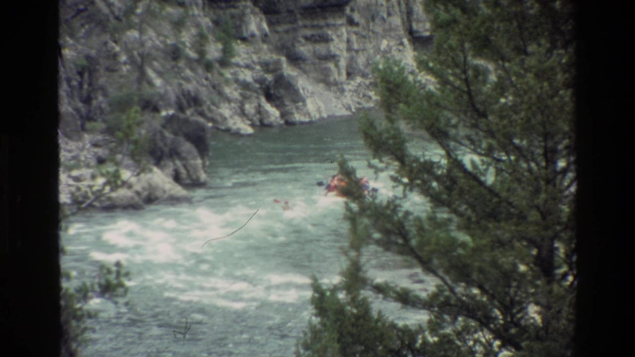 1980 8mm Grand Teton rafting scene with a red raft in rapids, rocky canyon walls, and evergreen trees partly obscuring the view.