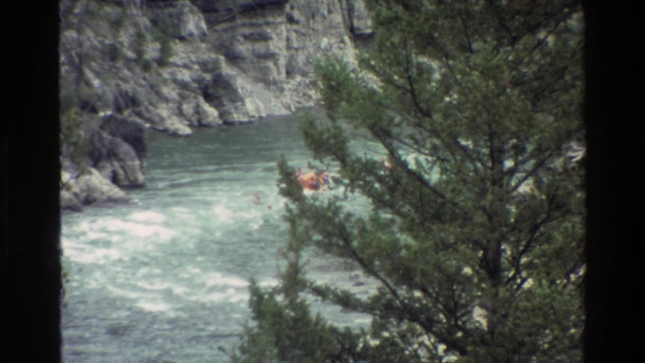 Raft in churning river water near canyon rocks and trees.