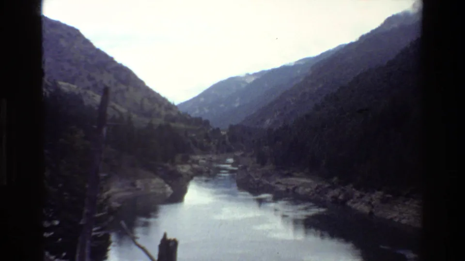 1980 8mm Grand Teton, Wyoming vista of a calm river valley framed by forested mountain slopes and dark film edges.