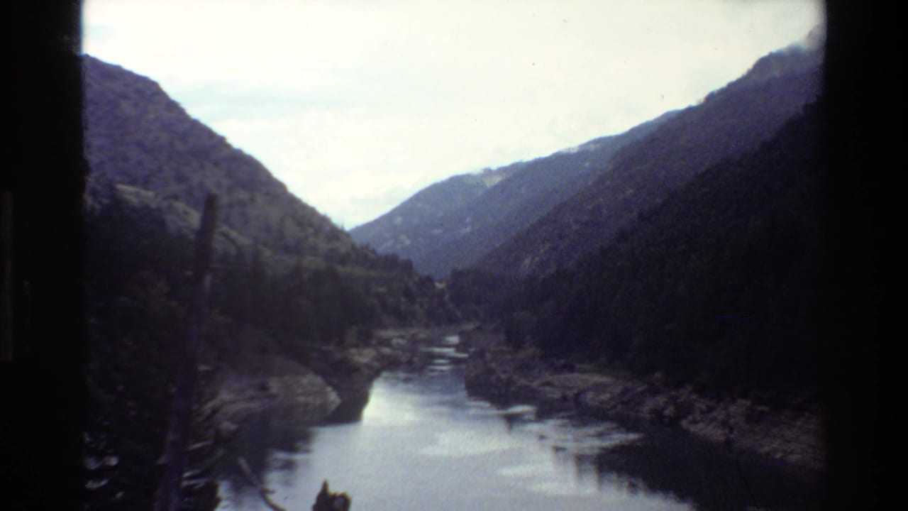 Forested mountain valley with reflective water and dark vertical frame edge.