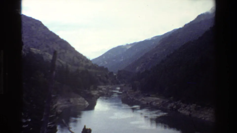 1980 8mm view of a Grand Teton river valley, with reflective water below steep wooded slopes and a dark window-like edge at center.