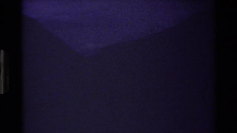 Underexposed 8mm transition frame with blue-purple cast and minimal readable subject detail.