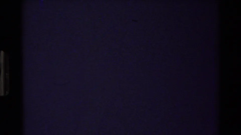 Mostly underexposed 8mm frame showing dark film area, gate edge, and faint side highlights during a transition.