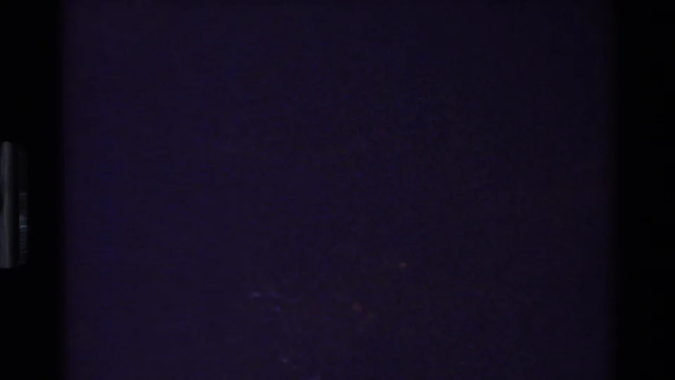 Near-black 1980 8mm end frame from the Grand Teton clip, with faint purple exposure and minimal visible forest detail.