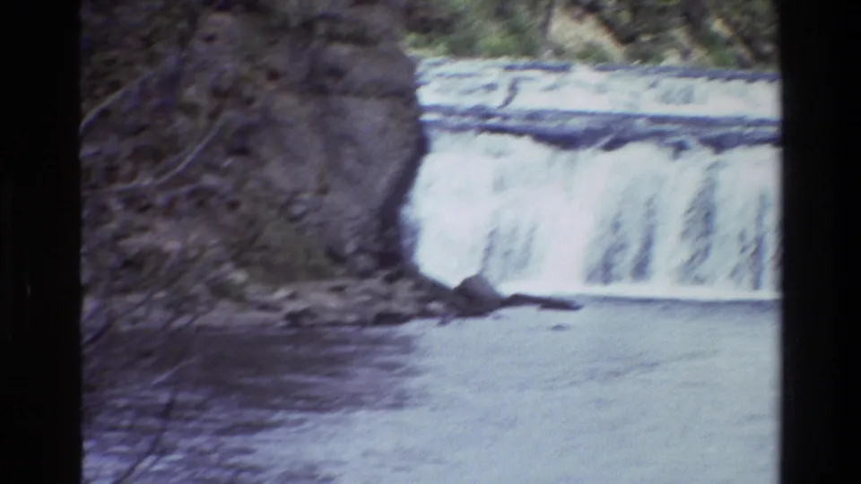1980 8mm frame showing whitewater spilling over a low waterfall with rock banks and forest in the Wyoming clip.