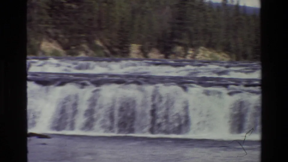 Home-movie frame of a broad low waterfall and river with dark forested banks in the Grand Teton, Wyoming metadata context.