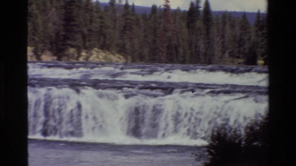 1980 8mm Grand Teton travel footage showing a broad waterfall and white water below a dense evergreen forest.
