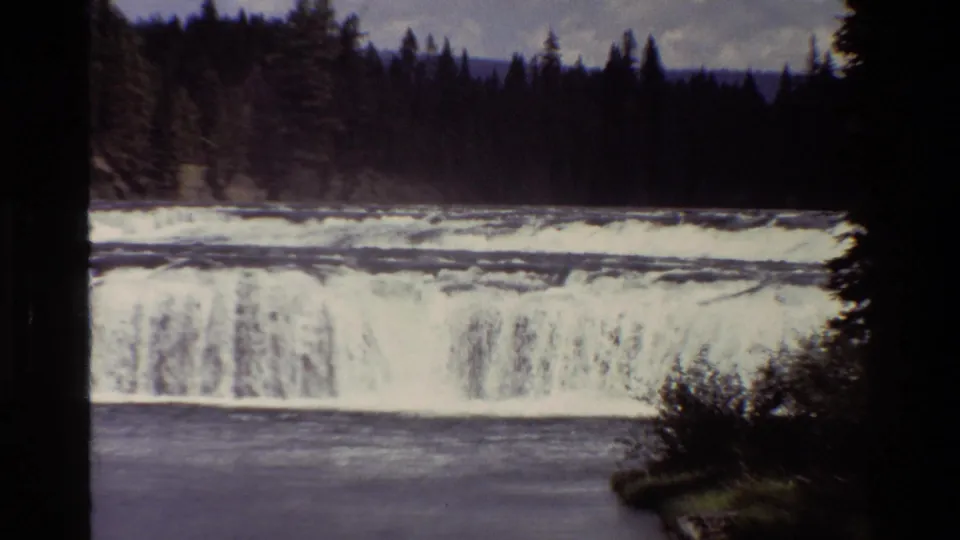 Vintage 8mm view of a forest-lined waterfall in Grand Teton, with white water dropping into a calmer river pool.