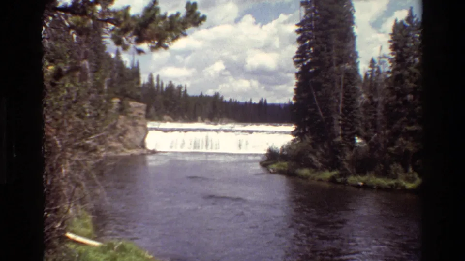 1980 home-movie view of a Grand Teton waterfall and river pool bordered by rock, evergreen trees, and low vegetation.