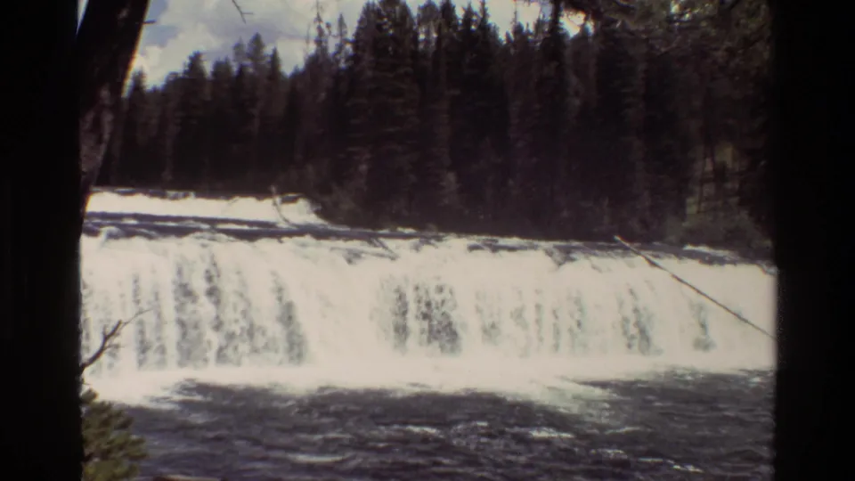 Grand Teton 8mm frame showing the waterfall closer in, with foaming water, dark river current, and pine forest behind it.
