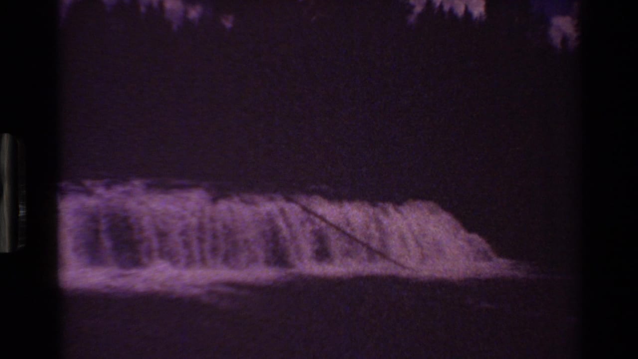 Dark, underexposed frame showing white water over a low waterfall.