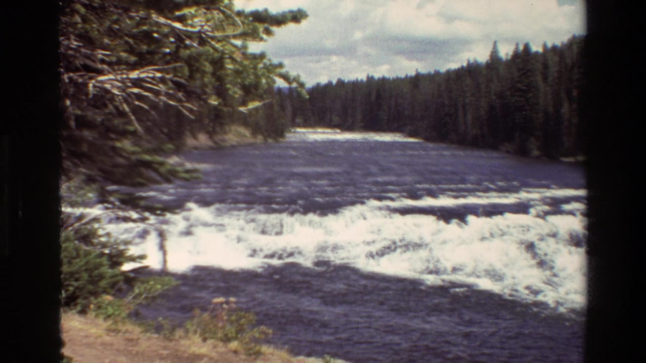 Grand Teton, Wyoming river scene with white rapids, dark water, evergreen banks, and cloudy sky in 1980 8mm footage.
