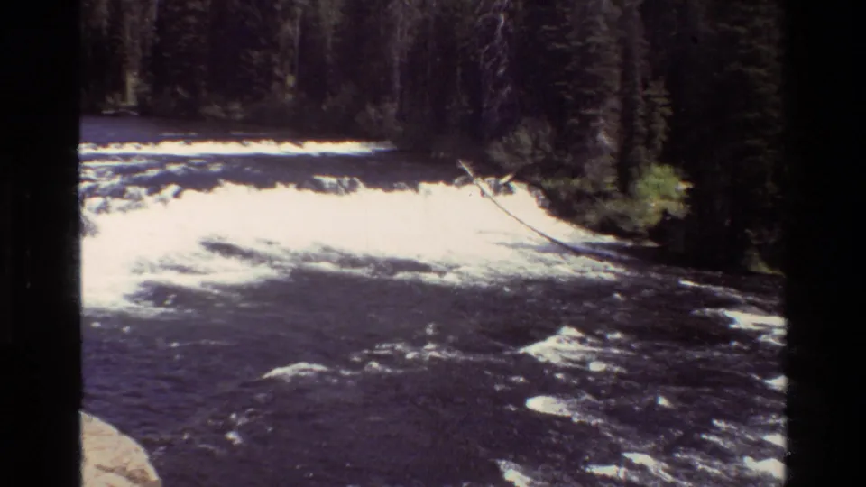 Grand Teton river rapids in 1980 8mm home-movie footage, with foaming water, dark current, evergreens, and a slanted branch.