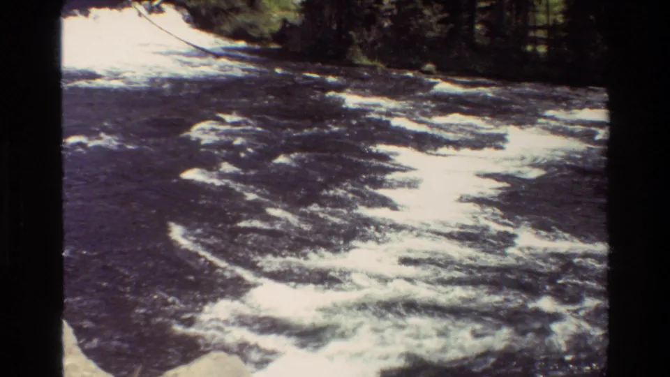 1980 Grand Teton 8mm frame of swift dark water and bright white foam moving past a wooded riverbank.