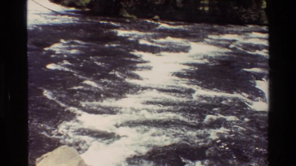 1980 Grand Teton 8mm frame showing a closer view of turbulent river rapids, dark water, pale foam, and forest behind.