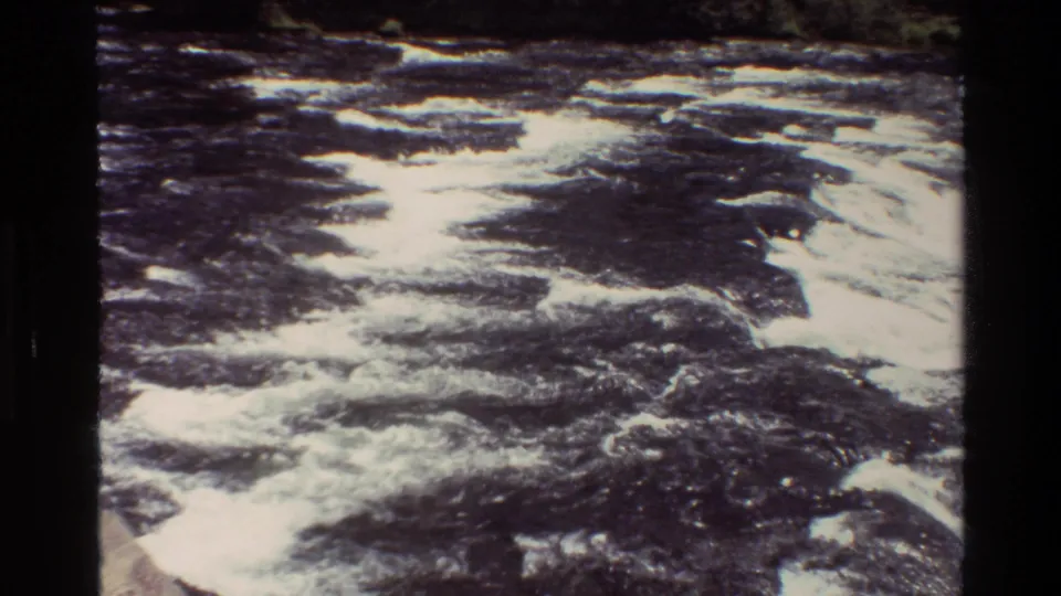 1980 Grand Teton 8mm frame with broad whitewater patterns across a dark river, framed by rocks and evergreen forest.