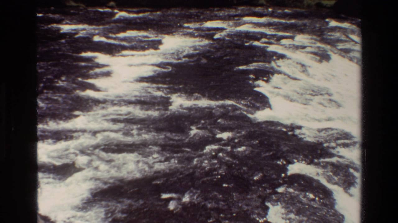1980 8mm home-movie frame from Grand Teton showing turbulent whitewater moving across dark rock and shadowed water.