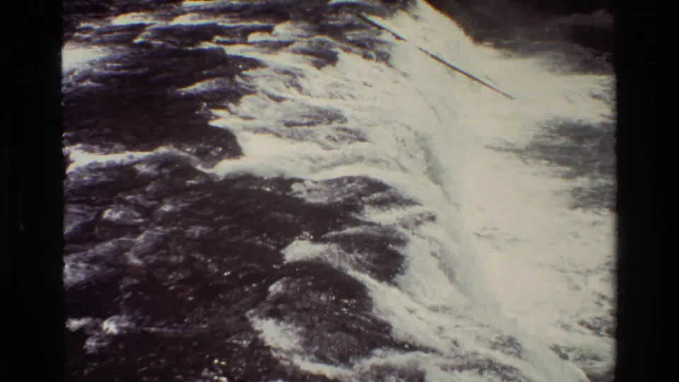 1980 Grand Teton home-movie frame showing whitewater flowing diagonally through a rocky river channel.