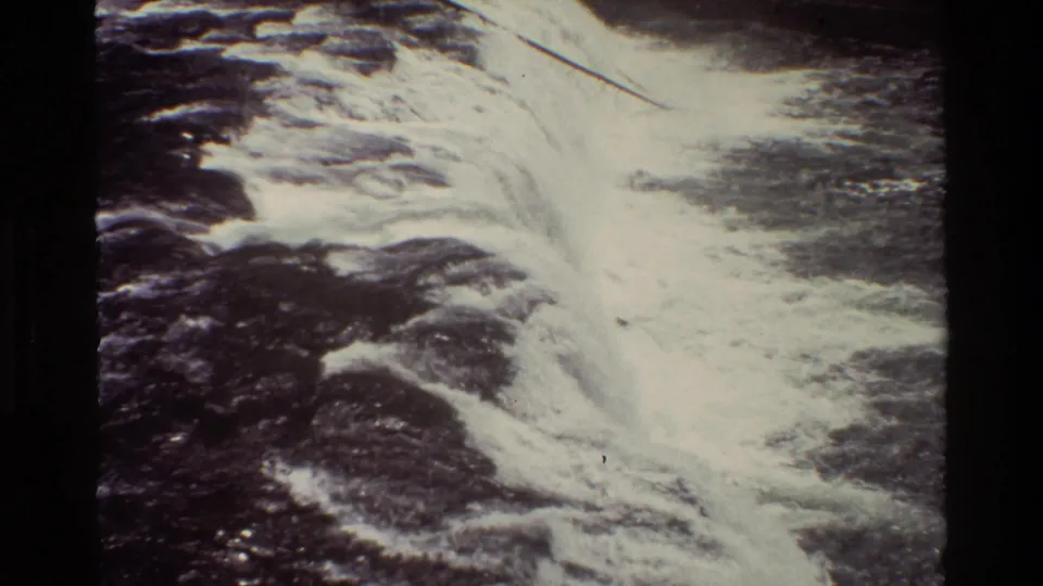 Soft 8mm frame from Grand Teton shows foamy whitewater spreading through dark rocks and flowing river water.