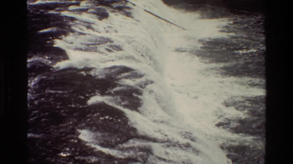 1980 8mm home-movie frame from Grand Teton metadata showing foamy waterfall water moving over dark rock.